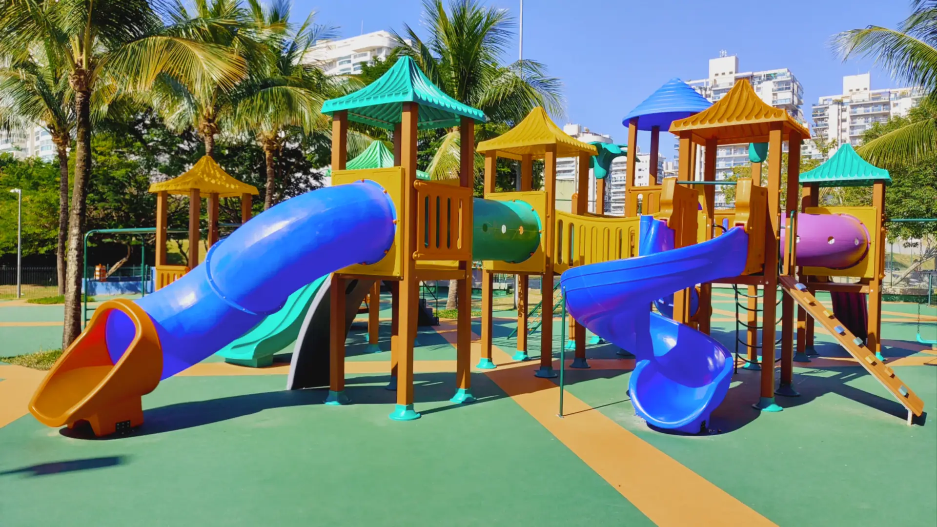 Playground com escorregadores em tubo azuis sobre piso emborrachado colorido na Associação Rio 2, Barra Olímpica